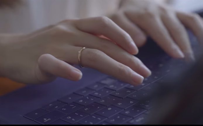 パソコンのキーボードを叩く女性と思しき手。右手の薬指には金色の指輪がはめられている。
